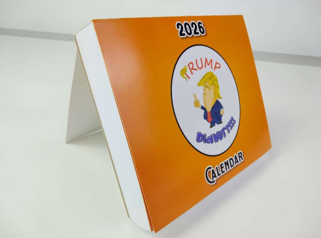 Trump Did WUT?!!! 2026 print calendar sitting on desk with stand.